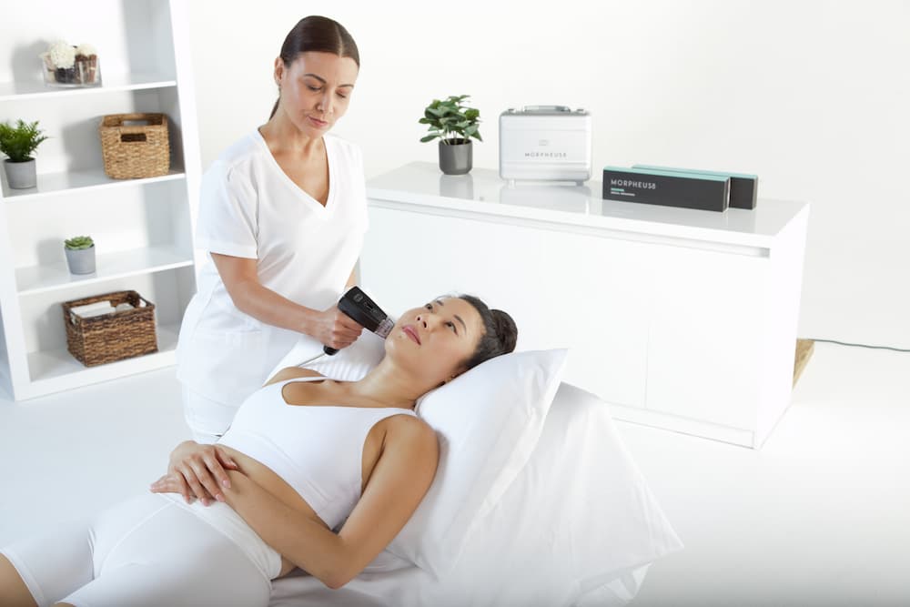 Aesthetic specialist performing a Morpheus8 body treatment on a woman to tighten and rejuvenate skin using RF microneedling technology.